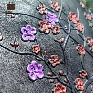 May include: Close-up of a black leather surface embossed with a floral design. The design features branches and flowers in shades of purple, red, and brown. The text "Leather Byusman" is in the upper left corner.