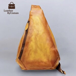 May include: A yellow-brown leather sling bag with a diagonal zipper and a strap. The bag has a triangular shape and a textured surface. The logo "Leather by Usman" is in the upper left corner.