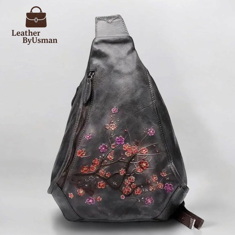 May include: A gray leather sling bag with a floral design in red and purple. The bag has a zipper closure and a brown strap. The brand name "Leather ByUsman" is visible in the upper left corner.