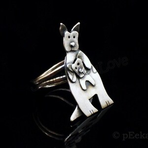 May include: A silver ring featuring a stylized kangaroo holding a joey in its pouch. The ring is a unique and charming piece of jewelry.