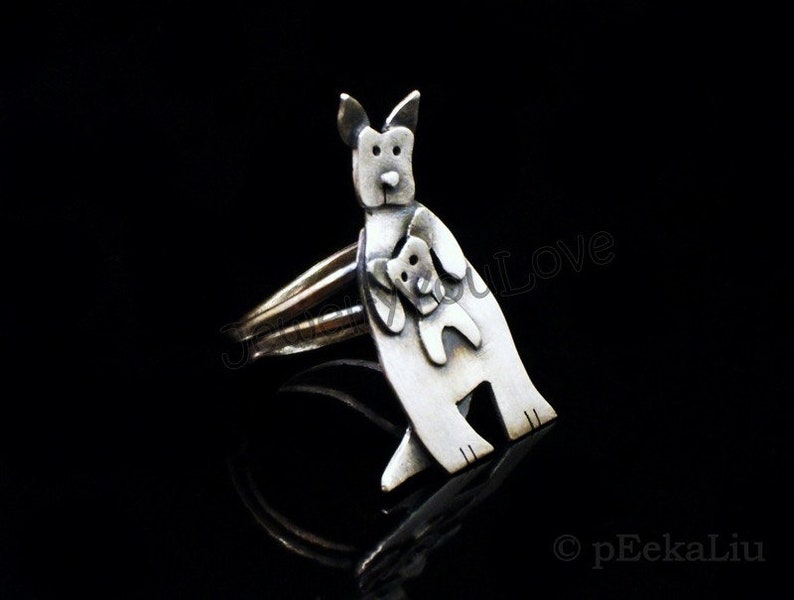 May include: A silver ring featuring a stylized kangaroo holding a joey in its pouch. The ring is a unique and charming piece of jewelry.