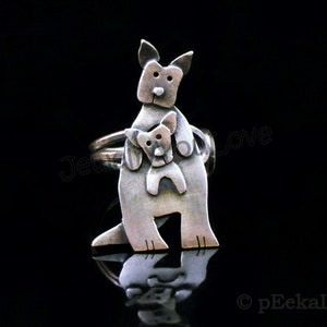 May include: A silver ring featuring a stylized kangaroo carrying a joey in its pouch. The ring is made of metal and has a textured finish.