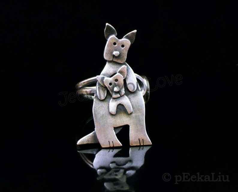 May include: A silver ring featuring a stylized kangaroo carrying a joey in its pouch. The ring is made of metal and has a textured finish.