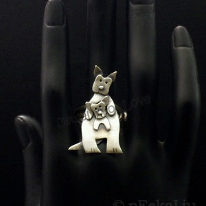 May include: A silver ring featuring a stylized kangaroo carrying a joey in its pouch. The ring is shown on a black mannequin hand.