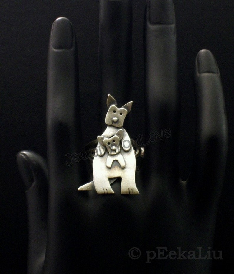 May include: A silver ring featuring a stylized kangaroo carrying a joey in its pouch. The ring is shown on a black mannequin hand.