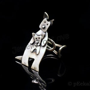 May include: A silver ring featuring a stylized design of two dogs, one carrying the other. The ring is made of metal and has a simple band.