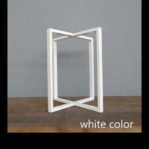 May include: White, geometric side table with an open, rectangular design. The table has an X-shaped base and a rectangular top. The text "white color" is at the bottom. The table is on a wooden surface.