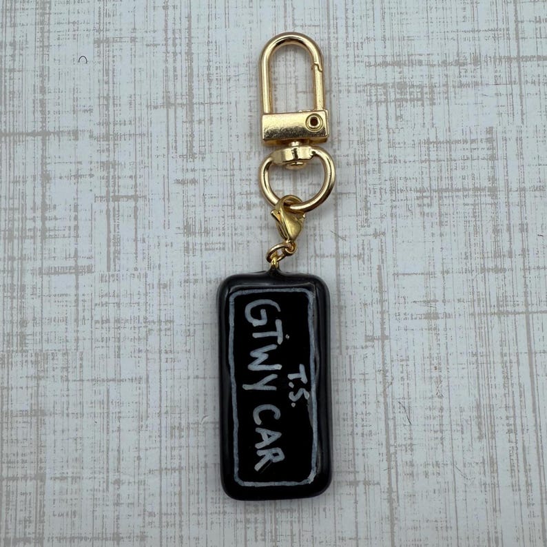 May include: A black rectangular keychain with the text "GTWY CAR" and "T.S." in white. The keychain has a gold-colored clasp and a small gold-colored ring.