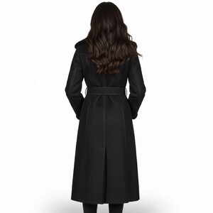 May include: A long, black coat with a belted waist and a split back. The coat has a faux fur collar and long sleeves. The person is facing away from the camera, showcasing the coat's design and fit. The coat is a classic style.
