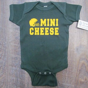 May include: A green baby onesie with a yellow football helmet and the text "MINI CHEESE" in yellow.