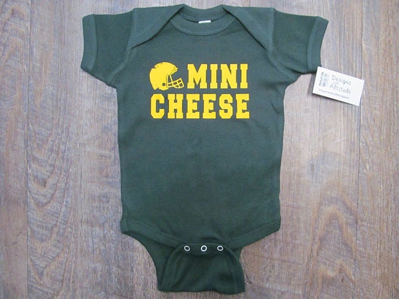 May include: A green baby onesie with a yellow football helmet and the text "MINI CHEESE" in yellow.
