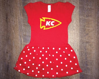 May include: Red and white polka dot dress with a yellow arrow with "KC" inside on the bodice.