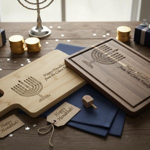 Puede incluir: Dos tablas de cortar de madera con un diseño de menorá y el texto "Happy Hanukkah from the Cohen Family". Una tabla es de color claro, la otra es oscura. También se muestran monedas de oro, dreidels y cajas de regalo.
