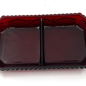 May include: A rectangular, divided dish in a deep ruby red color. The dish has a scalloped edge and a decorative pattern around the rim. The two compartments are square-shaped.