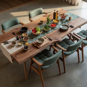 Op de afbeelding: Een houten eettafel met een levende rand, gedekt met een patroonloper, kommen met eten en servies. Vier groen gestoffeerde stoelen met houten frames zijn rond de tafel geplaatst. Bovenaanzicht.
