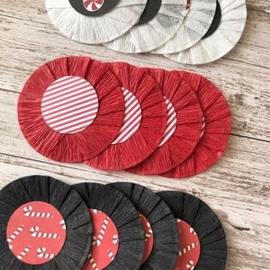 May include: A collection of decorative paper circles in white, red, and black. The white circles have black centers with candy cane designs. The red circles have white and red striped centers. The black circles have red centers with candy cane designs.