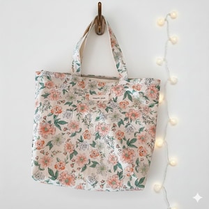 May include: A floral tote bag with a cream background and a pattern of pink, peach, and white flowers with green leaves. The bag has two handles and a small label that reads "simple wish".