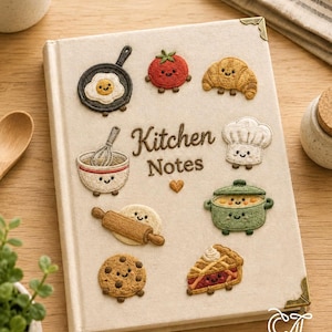 Könnte beinhalten: Ein cremefarbenes, stoffbezogenes Notizbuch mit der braunen Stickerei Kitchen Notes. Der Einband zeigt gestickte Aufnäher einer Pfanne mit Ei, Tomate, Croissant, Schneebesen in einer Schüssel, Kochmütze, Topf, Nudelholz, Keks und Kuchenstück.