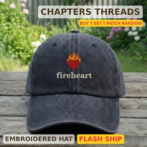 Puede incluir: Gorra de béisbol gris oscuro con la palabra "fireheart" bordada debajo de un corazón rojo con llamas. La gorra tiene una visera curva y el texto "CHAPTERS THREADS" está en la parte superior. La parte inferior de la gorra dice "EMBROIDERED HAT".