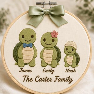 Könnte beinhalten: Ein runder hölzerner Stickrahmen mit Stoff, auf dem drei grüne Schildkröten gestickt sind. Die Schildkröten sind mit James, Emily und Noah beschriftet, darunter steht der Text The Carter Family. Oben ist eine salbeigrüne Satinschleife befestigt.