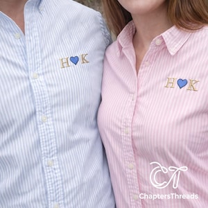 May include: Two button-down shirts, one light blue and one pink, with vertical stripes. Each shirt has embroidered initials "H♡K" in gold thread. The pink shirt has the "ChaptersThreads" logo at the bottom.