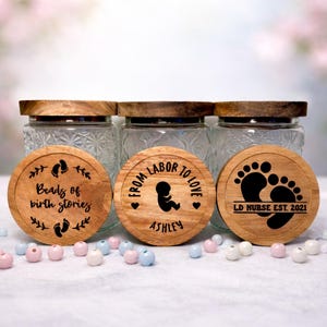 May include: Three glass jars with wooden lids and engraved wooden coasters. The coasters feature text and designs related to birth and babies, including footprints and the phrases "Beads of birth stories" and "From labor to love."