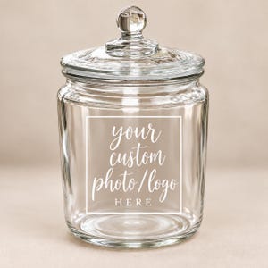 May include: A clear glass storage jar with a removable lid featuring a spherical knob handle. The front of the jar displays a white square frame containing the text: your custom photo/logo HERE in a mix of script and block lettering.
