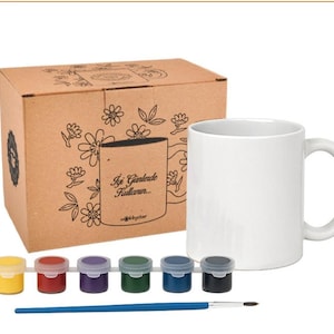 Può includere: Una tazza in ceramica bianca, vasetti di vernice gialla, rossa, viola, verde, blu e nera e un pennello sono esposti con una scatola marrone. La scatola presenta motivi floreali e testo in turco. Questo è un kit fai-da-te per dipingere tazze.