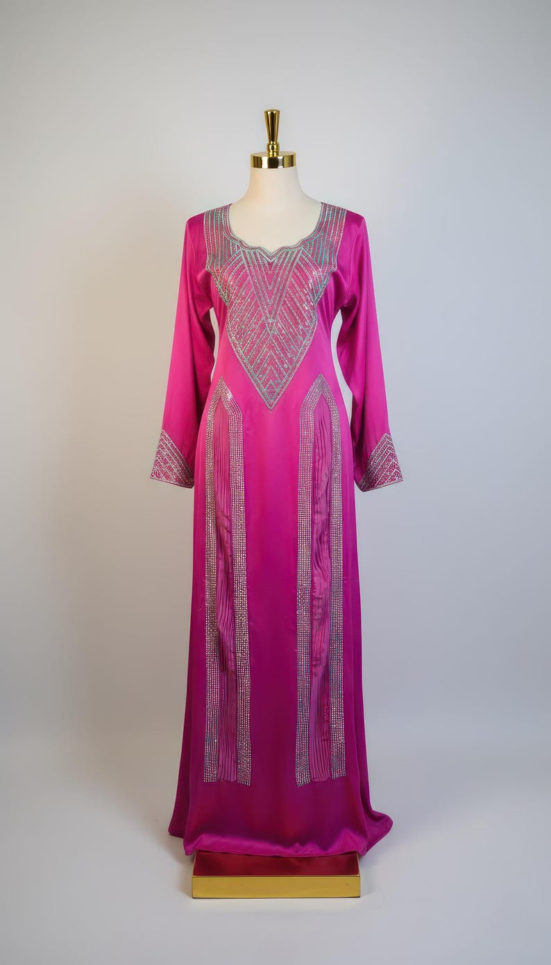 May include: A long, fuchsia-colored dress with long sleeves and a round neckline. The dress is embellished with silver-colored decorative accents on the neckline, sleeves, and front panels. The dress is displayed on a mannequin.