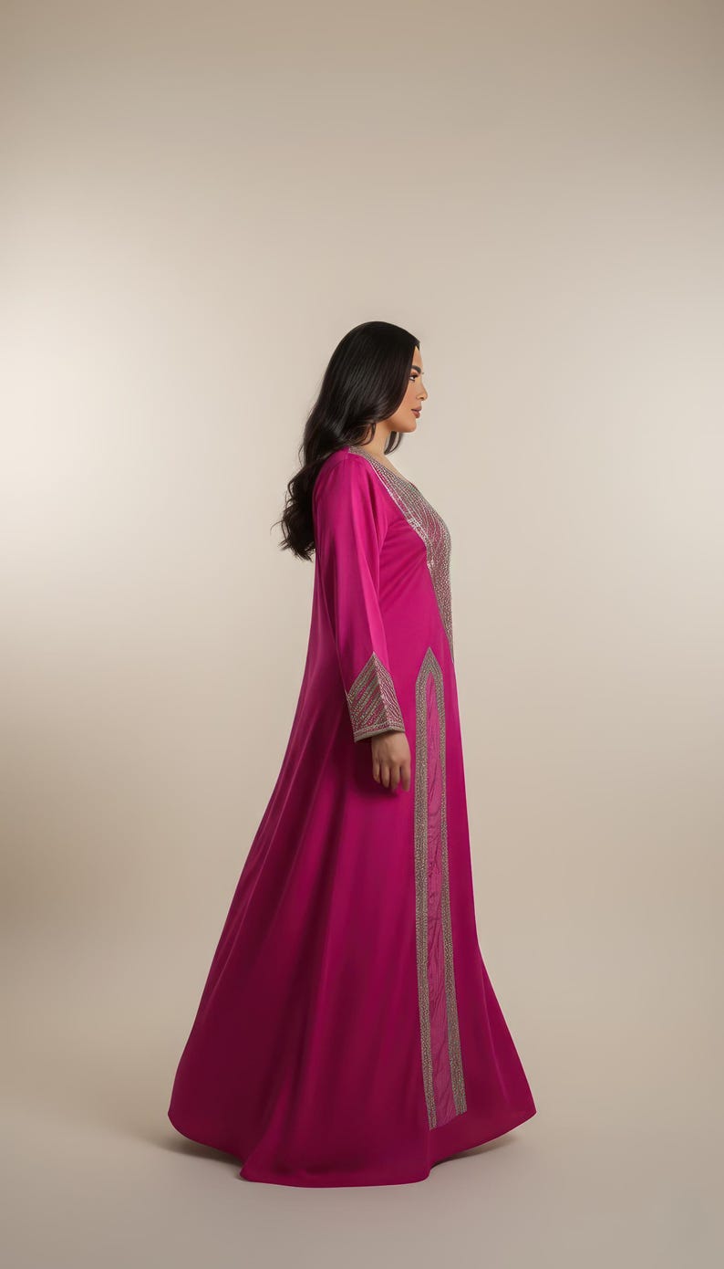 May include: A long, flowing magenta dress with long sleeves. The dress features intricate silver embroidery along the neckline, cuffs, and a vertical panel down the front. The dress is made of a soft, draping fabric.