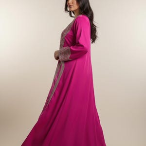 May include: A long, flowing magenta dress with long sleeves. The dress features intricate gold embroidery along the front and sleeves. The garment is made of a smooth, lightweight fabric, suitable for formal occasions.