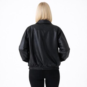 May include: A black leather jacket with a collared neckline and elasticized waist and cuffs. The jacket is shown from the back, with a woman wearing the jacket and black pants. The background is plain white.