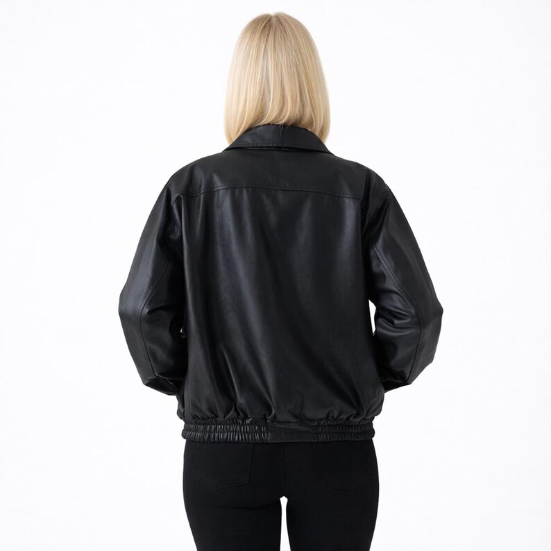 May include: A black leather jacket with a collared neckline and elasticized waist and cuffs. The jacket is shown from the back, with a woman wearing the jacket and black pants. The background is plain white.