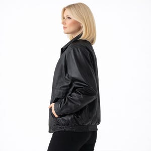 May include: A black leather jacket with a collared neckline, side pockets, and a ribbed hem. The jacket is worn by a person with blonde hair and is set against a white background.