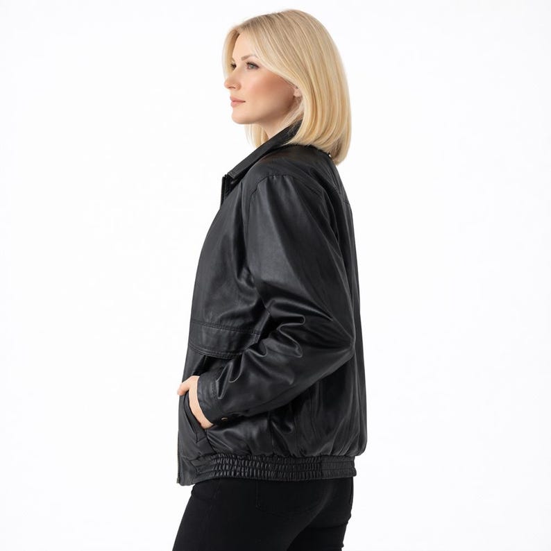 May include: A black leather jacket with a collared neckline, side pockets, and a ribbed hem. The jacket is worn by a person with blonde hair and is set against a white background.