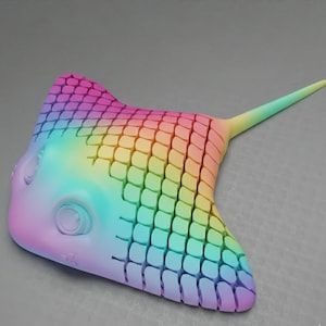 May include: A colorful, stylized stingray sculpture in a gradient of rainbow hues. The sculpture features a textured, scale-like pattern across its body and a long, pointed tail. The design is whimsical and eye-catching.