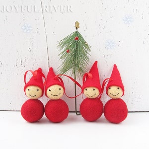 May include: Four red felt Christmas gnome ornaments with smiling faces and red pointed hats. Each ornament has a red ribbon for hanging. A small Christmas tree is behind the gnomes. The text "JOYFUL RIVER" is at the top.