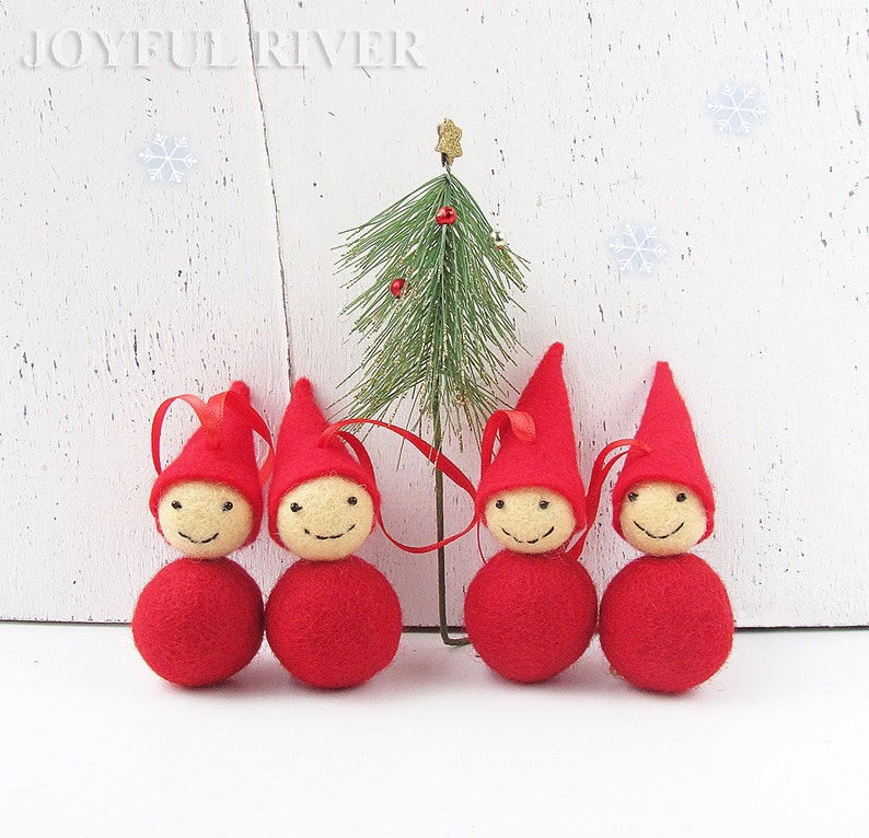 May include: Four red felt Christmas gnome ornaments with smiling faces and red pointed hats. Each ornament has a red ribbon for hanging. A small Christmas tree is behind the gnomes. The text "JOYFUL RIVER" is at the top.