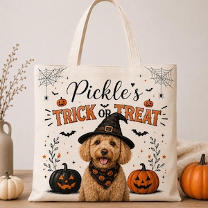 Pode incluir: Uma sacola de lona cor de creme com o gráfico de um cão dourado usando um chapéu de bruxa preto e uma bandana com estampa de abóbora. O texto diz Pickle's TRICK OR TREAT, cercado por ilustrações de aranhas, teias e abóboras.