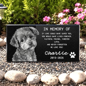 May include: A rectangular black memorial stone featuring a grayscale portrait of a puppy on the left and white engraved text on the right that reads: IN MEMORY OF IF LOVE COULD HAVE SAVED YOU, YOU WOULD HAVE LIVED FOREVER. FAITHFUL FRIEND, FOREVER LOYAL AND NEVER FORGOTTEN WE LOVE YOU! Charlie 2015-2026 with a paw print icon.