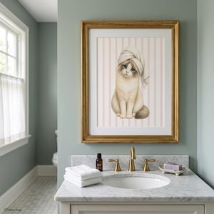 K&ouml;nnte beinhalten: Ein gerahmter Druck mit einer Katze, die ein Handtuch auf dem Kopf tr&auml;gt, vor einem rosa-wei&szlig; gestreiften Hintergrund. Das Kunstwerk befindet sich in einem goldenen Rahmen und h&auml;ngt &uuml;ber einem Badezimmerwaschbecken. Die Katze hat blaue Augen und einen flauschigen Schwanz.