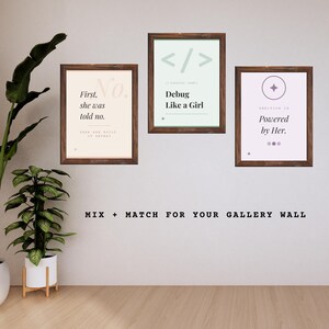 Pode incluir: Três impressões de arte emolduradas com citações inspiradoras. As impressões têm molduras de madeira marrom e apresentam textos como "First, she was told no", "Debug Like a Girl" e "Powered by Her". As impressões são exibidas em uma parede branca.