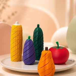 Può includere: Una collezione di cinque oggetti a forma di verdura che include una pannocchia di mais gialla, una melanzana viola, un cetriolo verde scuro, un peperone arancione e un pomodoro rosso, disposti su un piatto bianco con una finitura opaca e liscia.