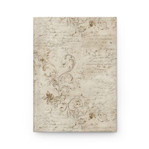 May include: A rectangular journal with a vintage design. The cover features a cream-colored background with faded script and floral scrollwork in shades of brown and beige. The journal is blank.