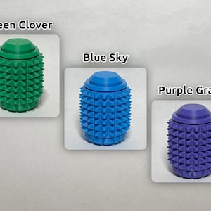 May include: Three cylindrical sensory fidget tools with a textured, spiked surface. The green one is labeled Green Clover, the blue one is labeled Blue Sky, and the purple one is labeled Purple Grape. Each item features a smooth, flat circular top.