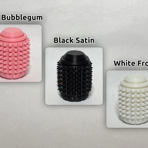 May include: Three cylindrical objects with a textured, spiked surface and a smooth top cap. The items are labeled Pink Bubblegum in pink, Black Satin in black, and White Frost in white. Each object features a repeating pyramid stud pattern.
