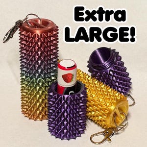 May include: A collection of cylindrical, spiked containers with metal keychains, featuring a gradient of metallic colors including copper, gold, and purple. One container holds a lip balm tube with a strawberry graphic. Text reads: Extra LARGE!