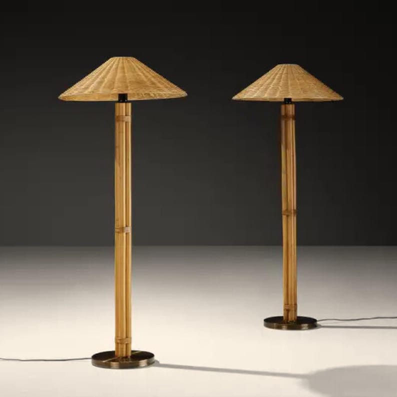 May include: Two bamboo floor lamps with woven shades. The lamps have a natural wood finish and a circular base. The shades are a light tan color and are square-shaped. The lamps are on a white surface.
