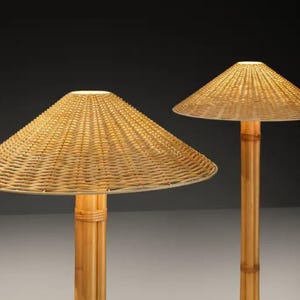 May include: Two lamps with conical woven rattan shades and bamboo poles. The lampshades are a light beige color, and the bamboo poles are a natural light brown. The lamps are lit, emitting a warm glow. The lamps are decorative and suitable for indoor use.