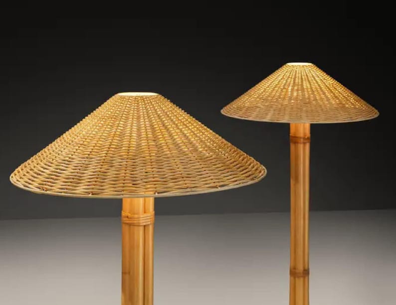 May include: Two lamps with conical woven rattan shades and bamboo poles. The lampshades are a light beige color, and the bamboo poles are a natural light brown. The lamps are lit, emitting a warm glow. The lamps are decorative and suitable for indoor use.